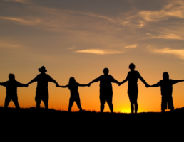 People of all ages holding hands in a field at sunset