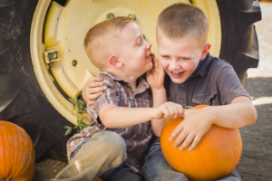 Two boys playing with pumpkins, near a parked tractor