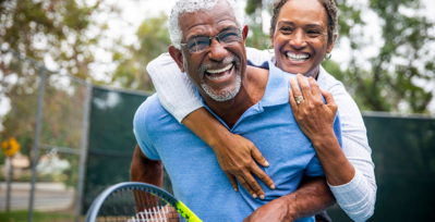 Older couple hugging and smiling while they play tennis