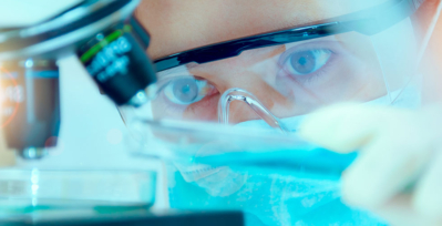 Person in lab gear looking into a microscope