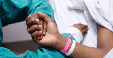 Someone in scrubs holding the hand of someone wearing a hospital bracelet.